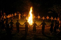 Children in scout uniforms hold hands around a bonfire