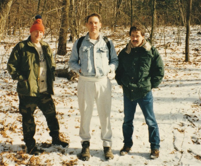 Three men standing on a snowy trail in the woods