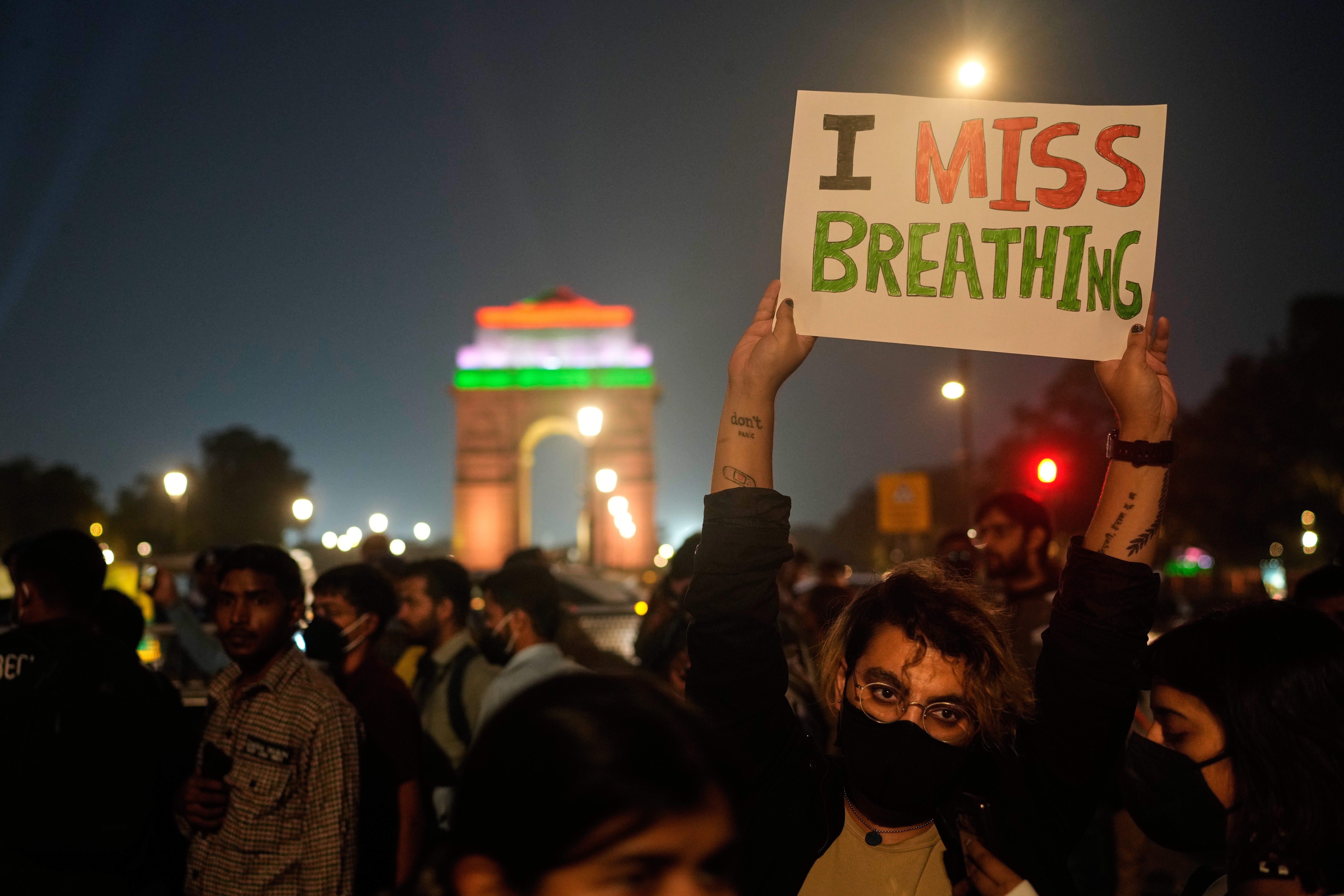 Protesters gather in a public plaza, with one holding a sign that reads 'I miss breathing.'