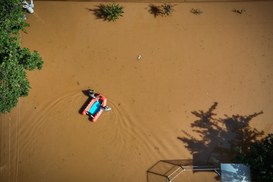 An aerial view of two people wading through floodwater, guiding a small inflatable boat