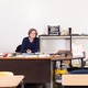 An English teacher sits at a desk in an empty high school classroom