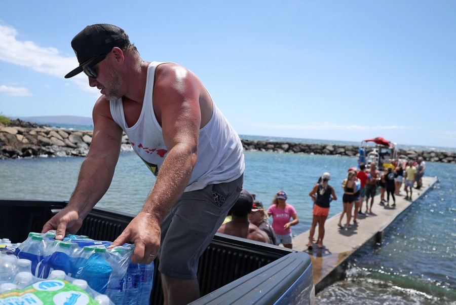 Volunteers form a brigade to load cases of drinking water along a dock onto a small boat.