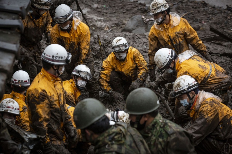 About a dozen rescue workers are seen standing in and digging in thick mud.