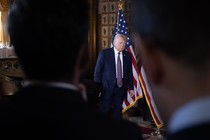 Donald Trump stands during his press conference between the silhouettes of two men in the crowd