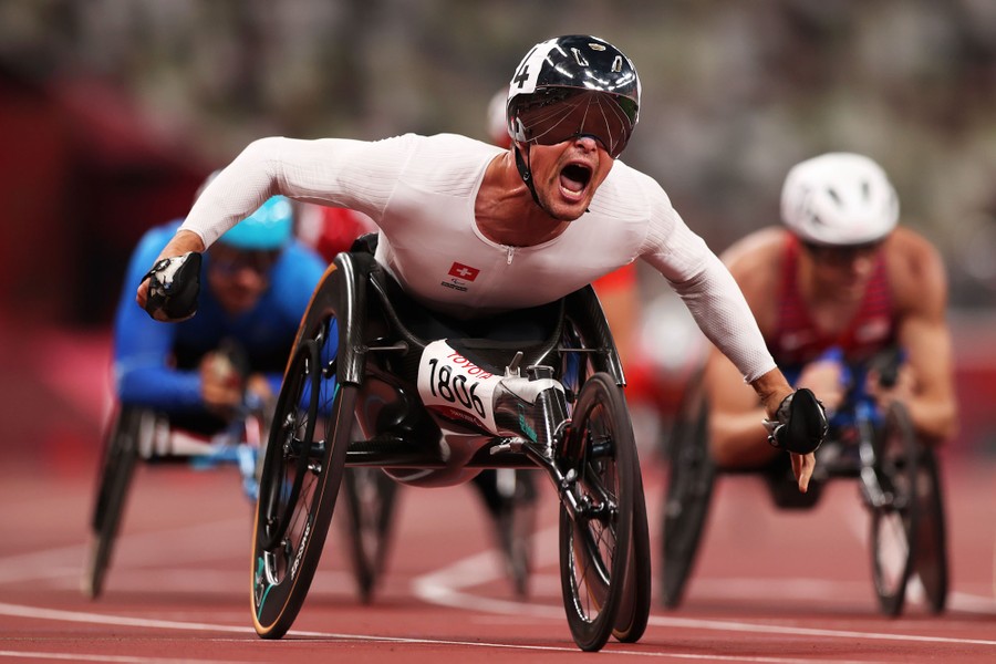 Several men in wheelchairs cross the finish line on a racetrack.