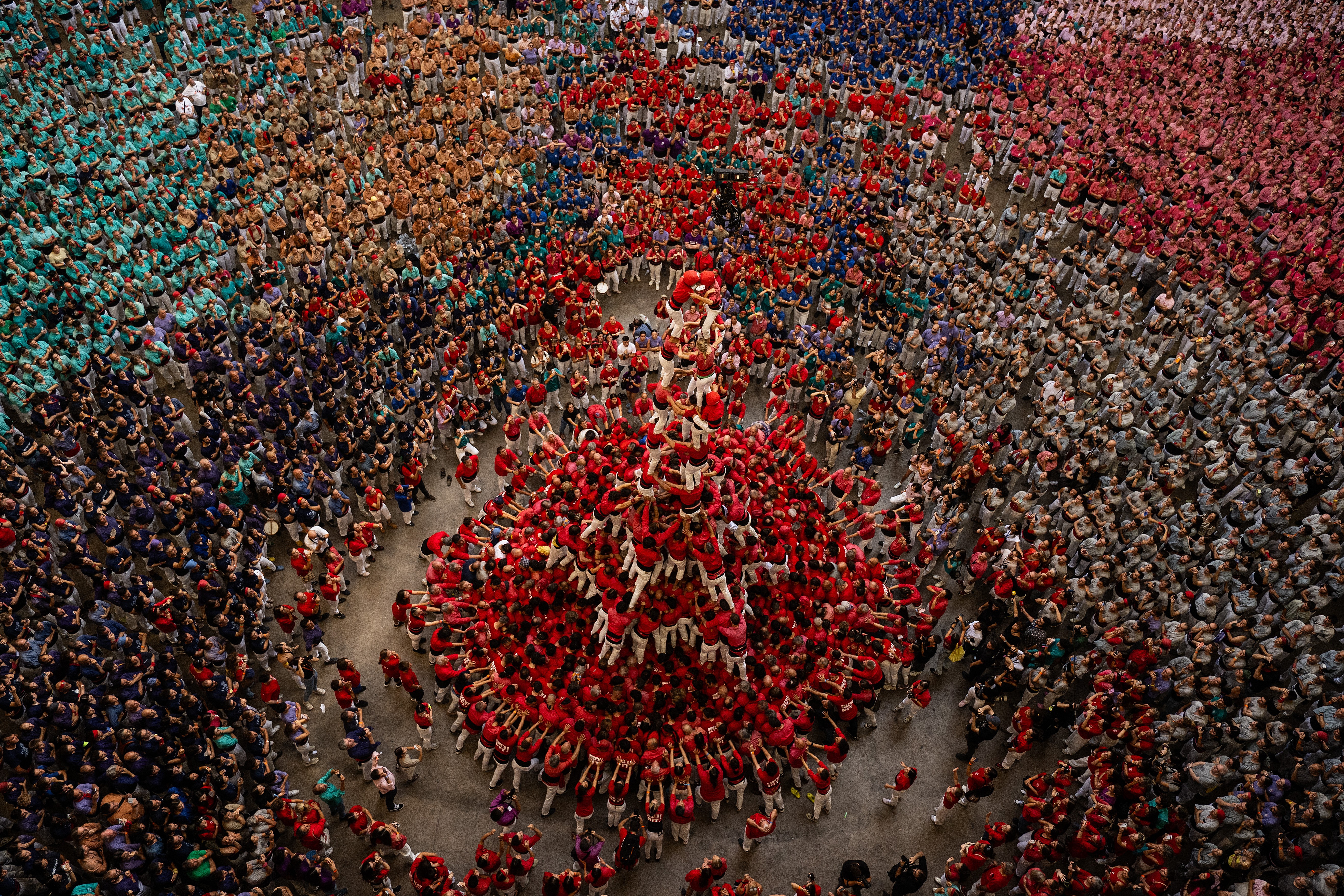 An overhead view of competing teams watching as one team forms a human tower in an arena