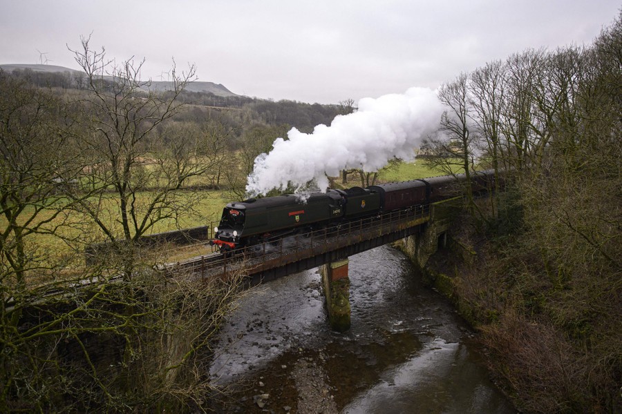 A steam train crosses a small bridge in a green valley.