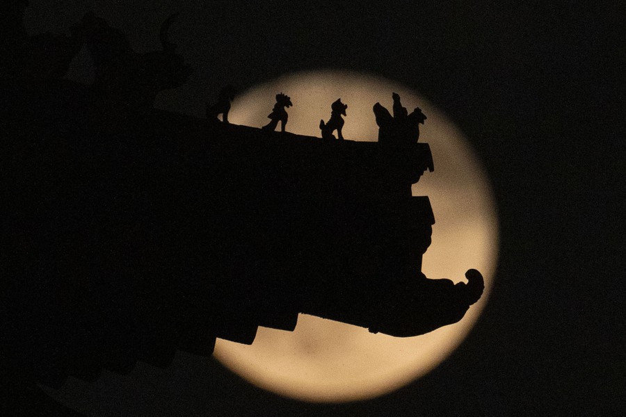 Roof decorations on a tower are silhouetted against a full moon.