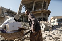 A man walks past a house destroyed during fighting between Iraqi security forces and Islamic State's fighters in Mosul, Iraq, carrying a wheelbarrow loaded with possessions. 