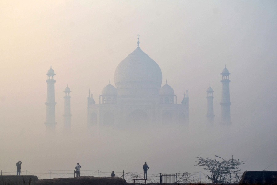 People look toward the Taj Mahal on a cold and foggy morning.
