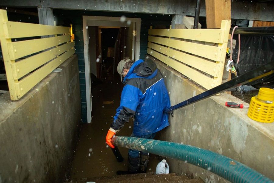 A person carries a large hose into the flooded basement of a house.