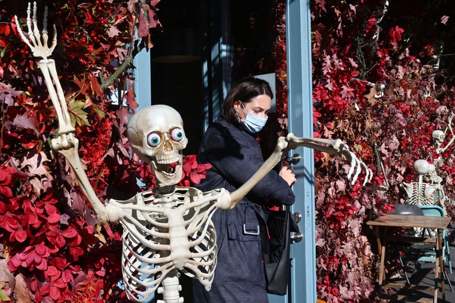 A woman wearing face mask leaves a restaurant decorated with skeletons.