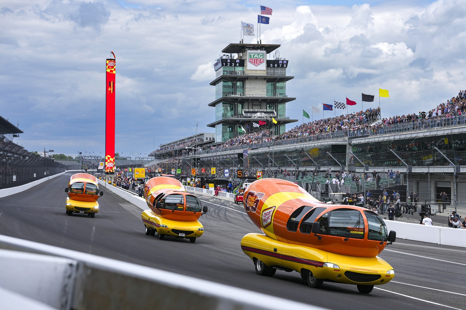 Three wienermobiles are seen driving down a racetrack.