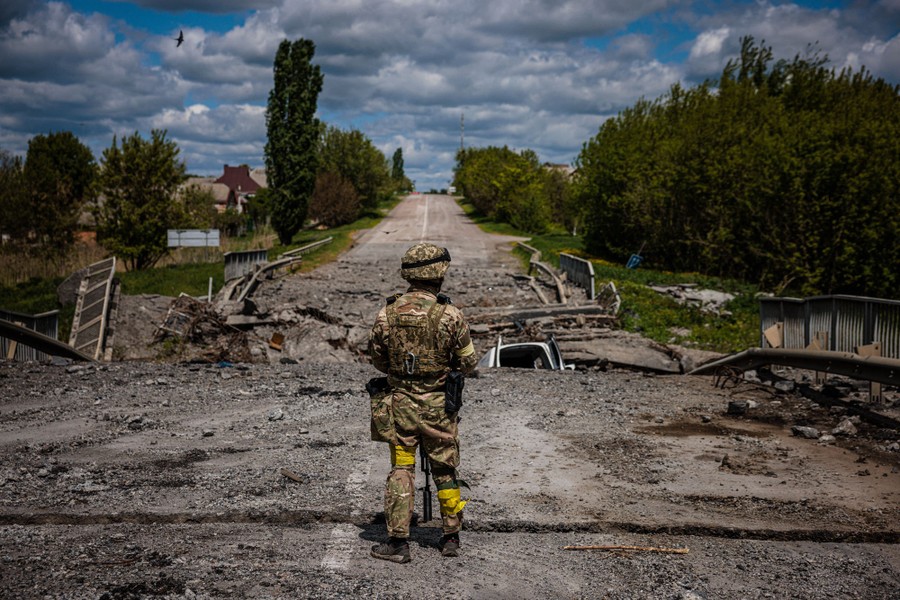 A soldier stands in a road looking at a destroyed bridge just ahead.