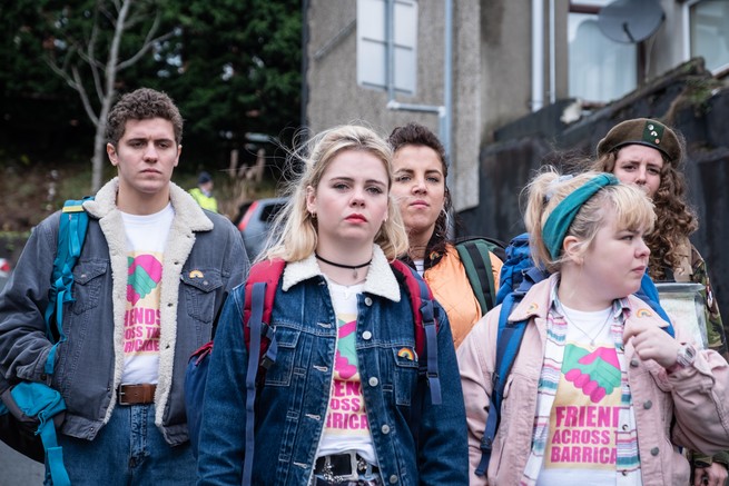 The five main characters in "Derry Girls" walking somberly down a neighborhood street