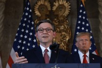 House Speaker Mike Johnson speaks at the podium and Donald Trump stands behind him