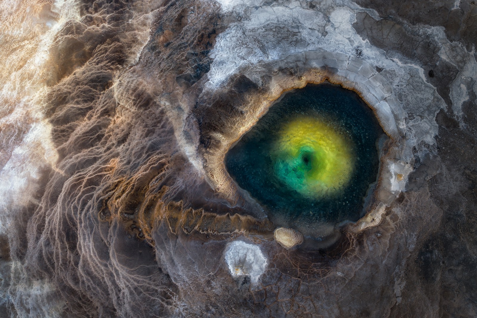 An aerial view of a colorful geothermal pool, looking like the eye of some fearsome creature.