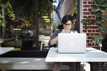 A young man looks thoughtfully at a laptop while sitting at a cafe