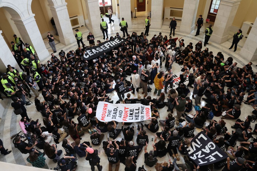 A large crowd of protesters calling for a ceasefire in Gaza sits on the floor inside a building.