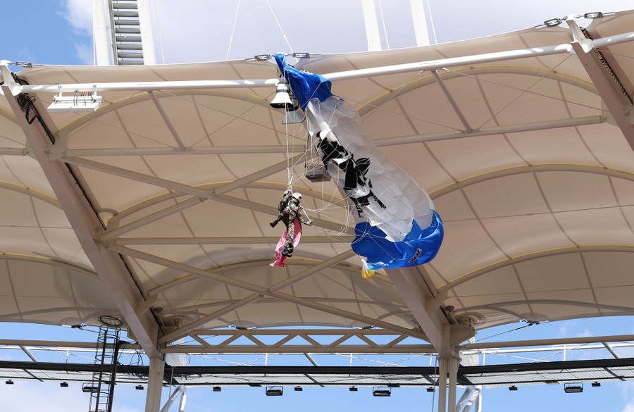 A person hangs from tangled lines of a parachute that have been snagged by the roof of a stadium.