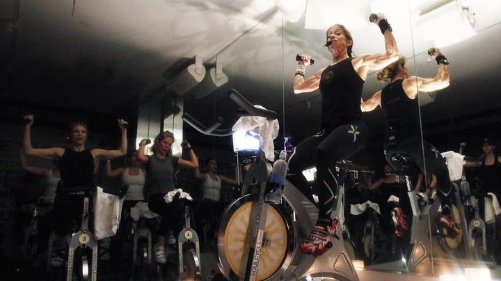 A woman lifts weights while riding a SoulCycle stationary bicycle.