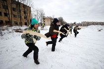 A half-dozen civilians in cold-weather gear run across a field carrying wooden replicas of rifles.
