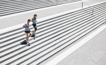 A man and woman jog down cement stairs together.