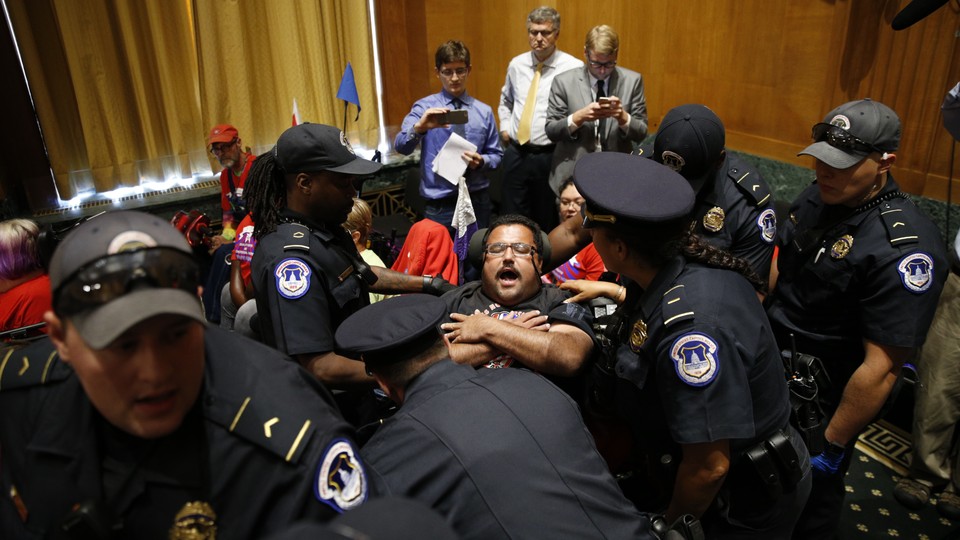 A police officer removes a disabled protester form a Congressional hearing.