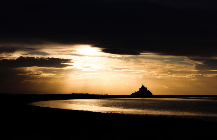 A cluster of buildings sits atop a small island in the distance, silhouetted by low sunlight.