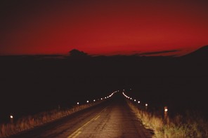 A photograph of a road going into Big Bend National Park during near dark, under a red sky