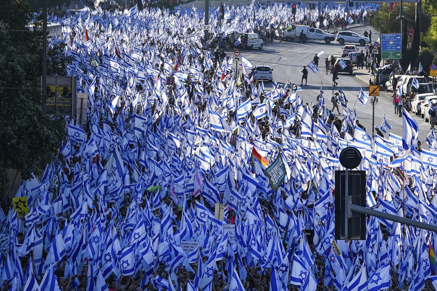 A large crowd of demonstrators carrying Israeli flags marches down a street.