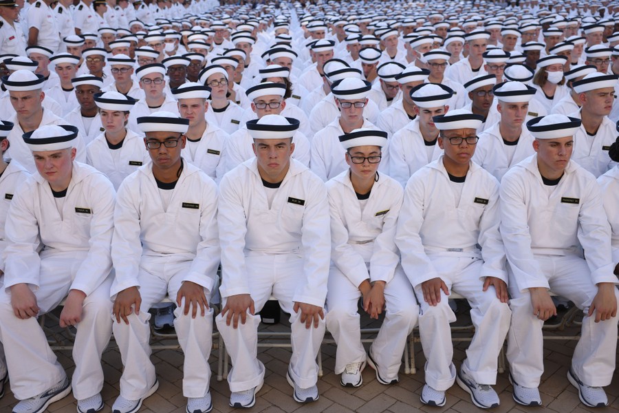 Hundreds of new members of the U.S. Naval Academy sit together in rows.