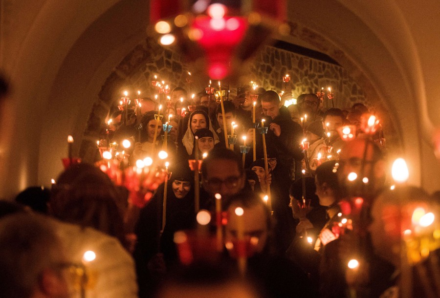 People walk together in a monastery hallway, carrying lit candles.