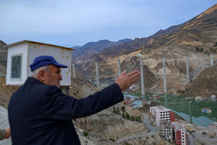A person holds up one arm while looking into a valley that is being flooded.