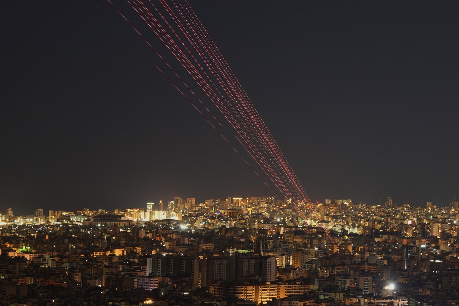 Streaks of light from tracer rounds fired into the sky, seen above a city at night.