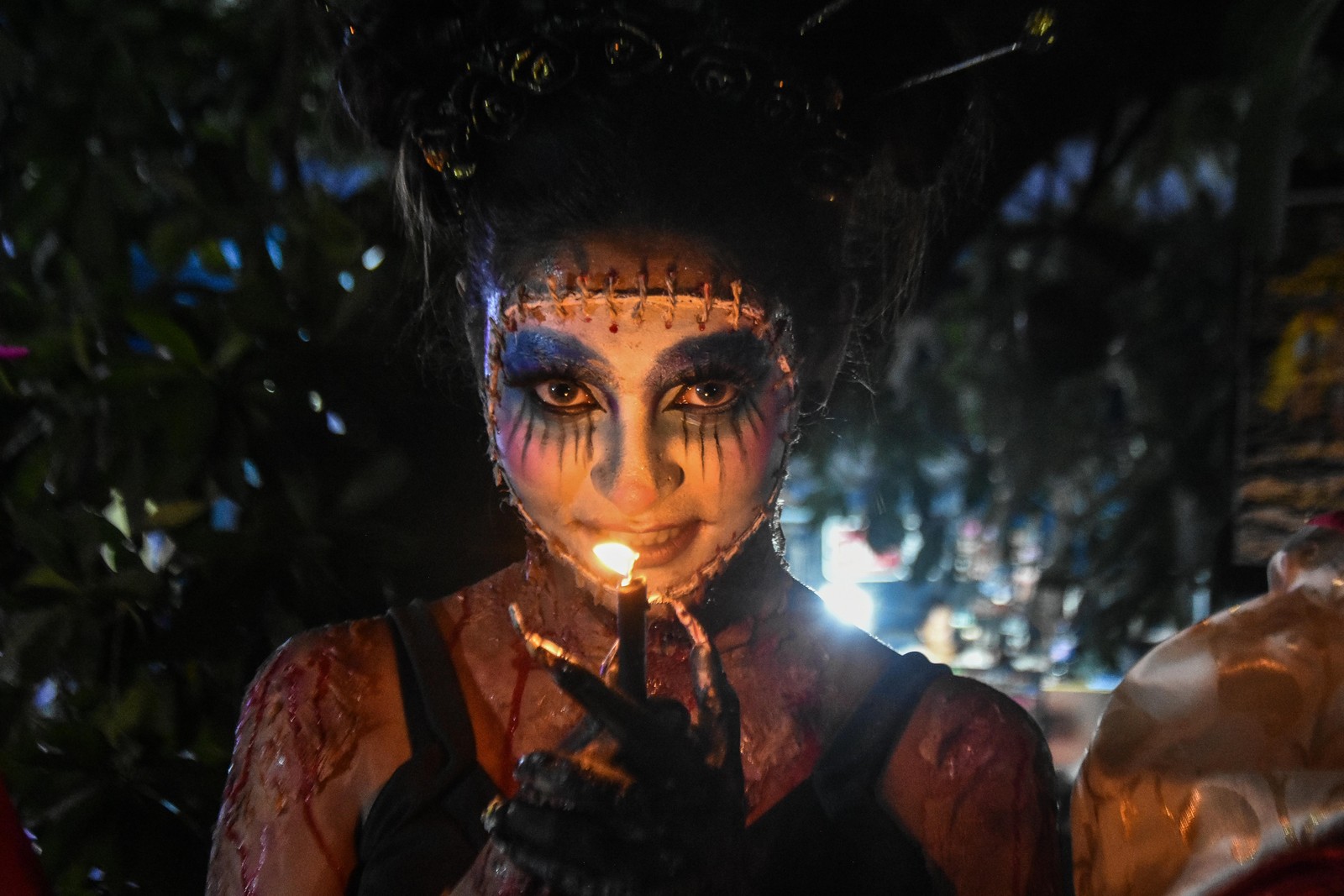 A person in frightening makeup smiles while holding a candle near their face.