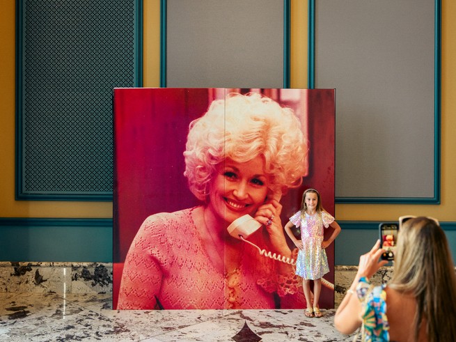 a young girl takes a photo in front of a Dolly Parton poster