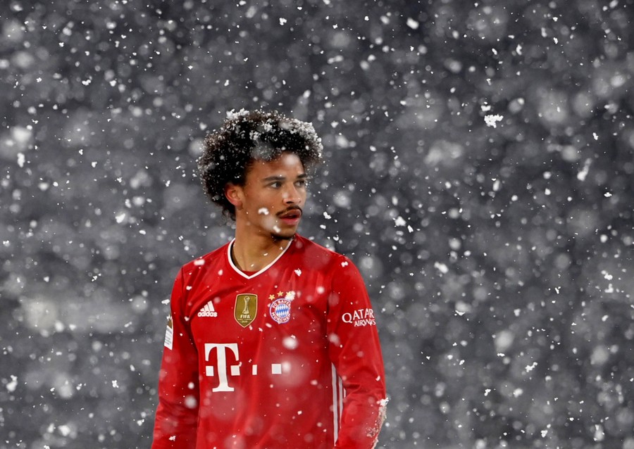 A soccer player stands amid falling snowflakes.