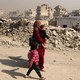 A Palestinian mother walks with two children beside rubble in Gaza.