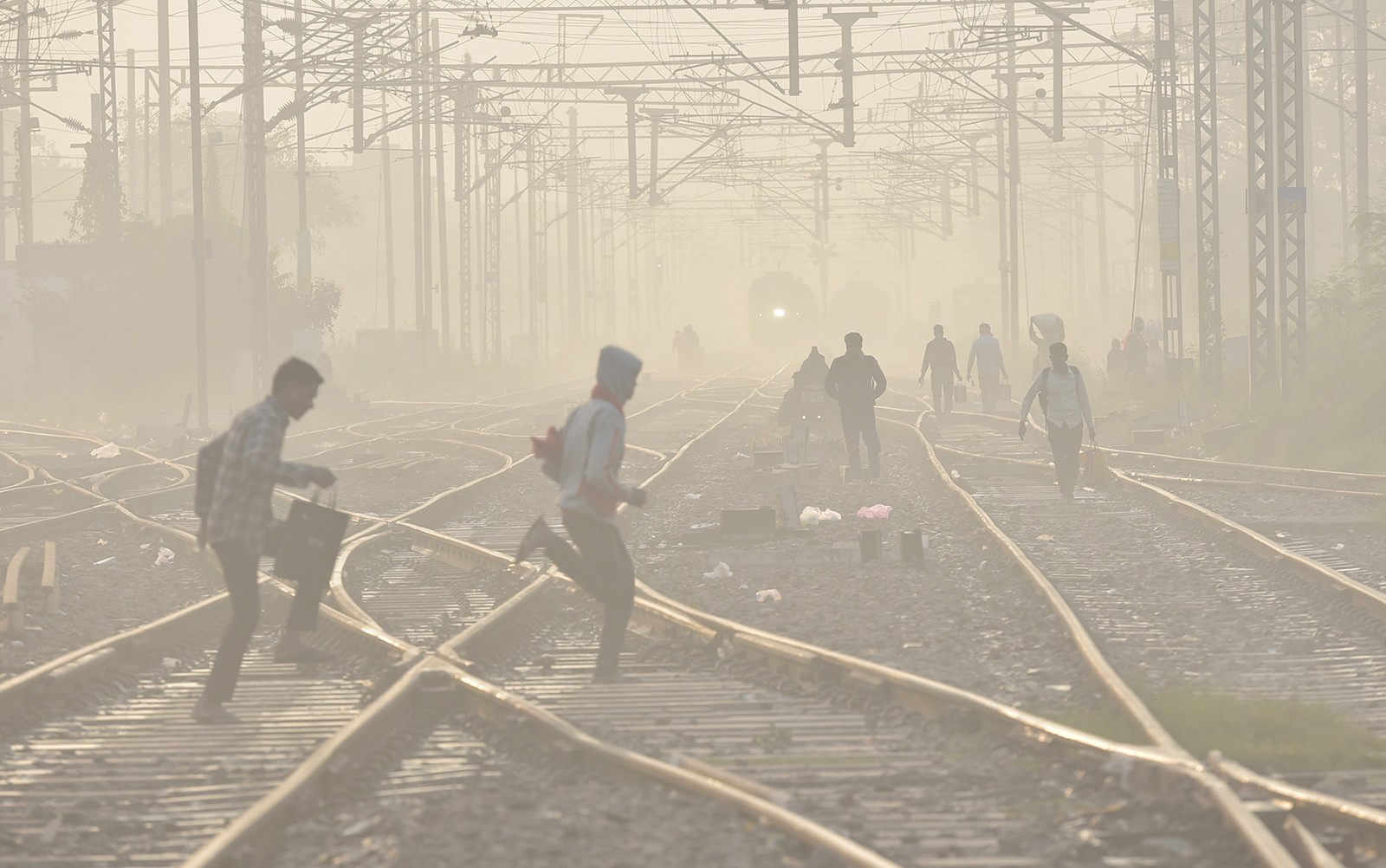 People walk through a rail yard, crossing tracks on a smoggy day.