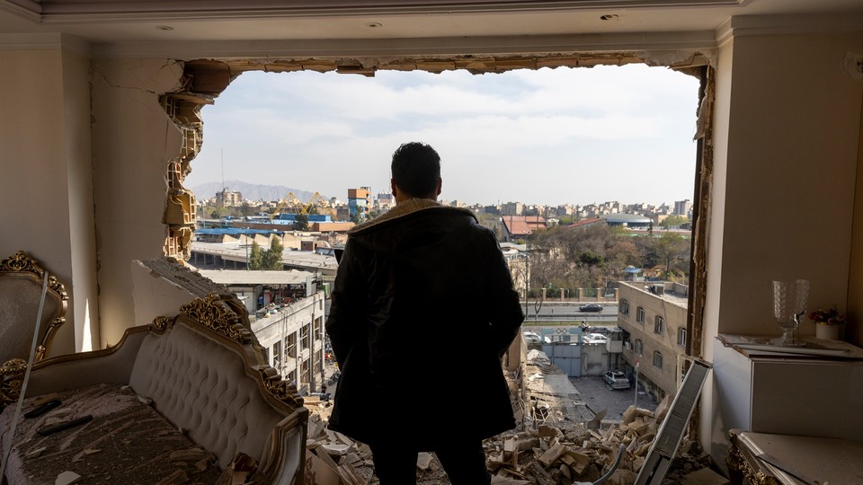 Photograph of a man looking through the side of a bombed out building.