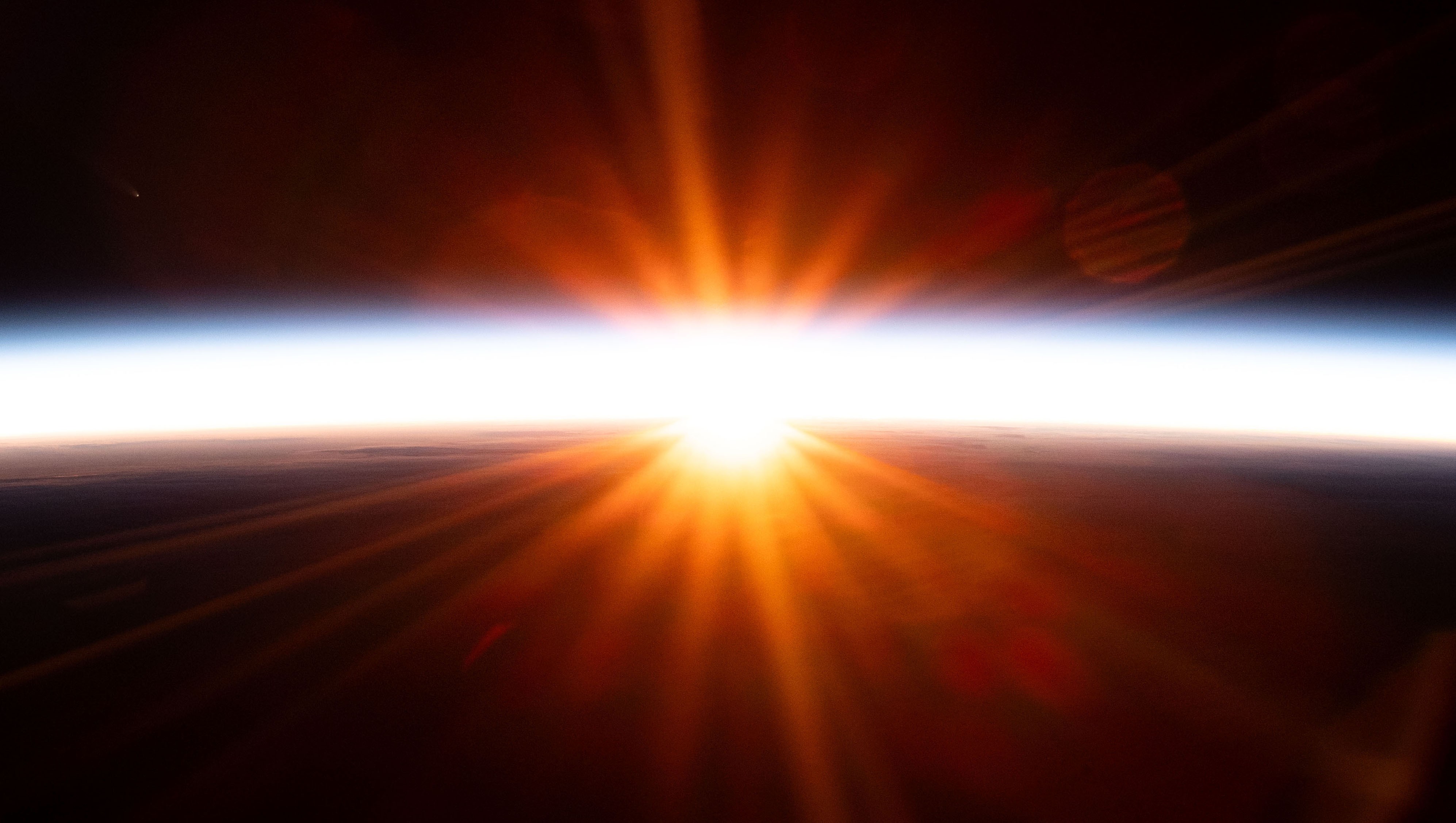 The sun glows and radiates light, appearing along Earth’s horizon, seen from orbit.
