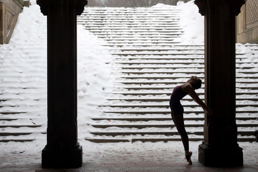 A ballerina poses between columns in Central Park on a snowy day.
