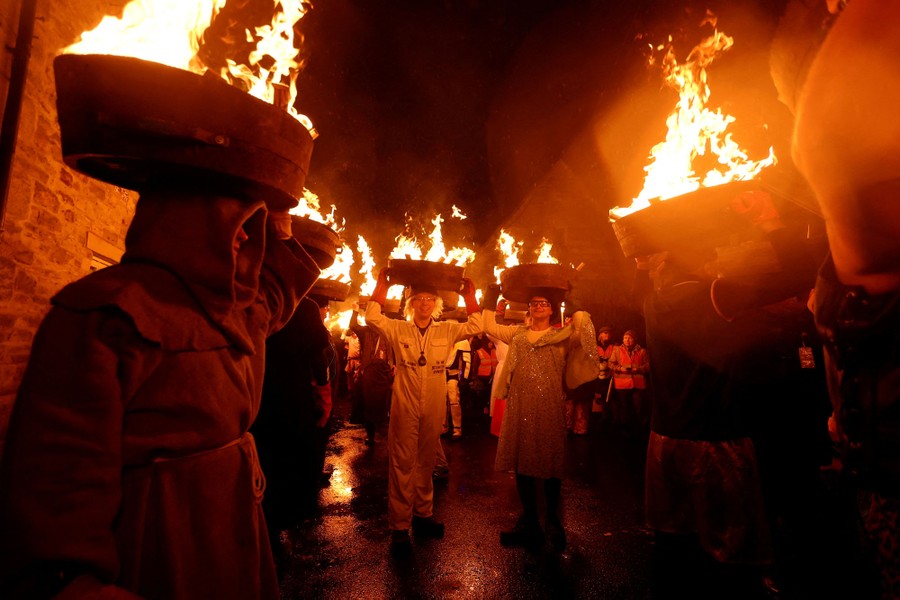 Revelers carry the flaming bottoms of barrels on their heads, while parading down a narrow street.