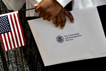 Photograph of hands holding a U.S. flag and an envelope labeled “U.S. Citizenship and Immigration Services”