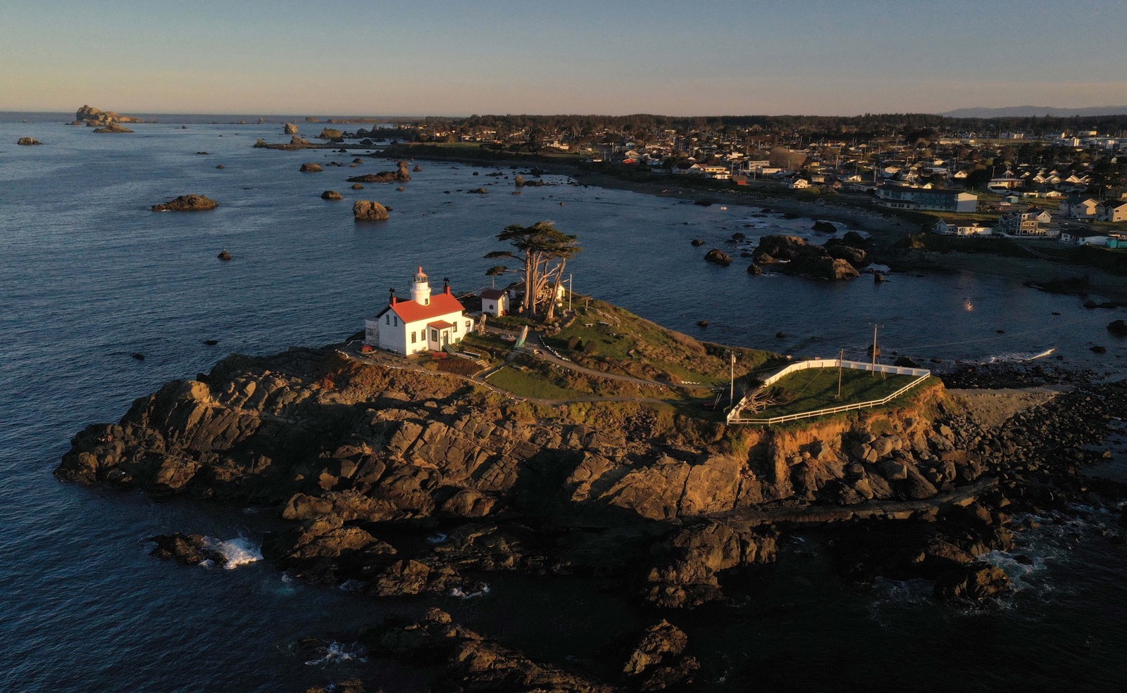 An aerial view of a lighthouse and rock formations beside a small city in northern California