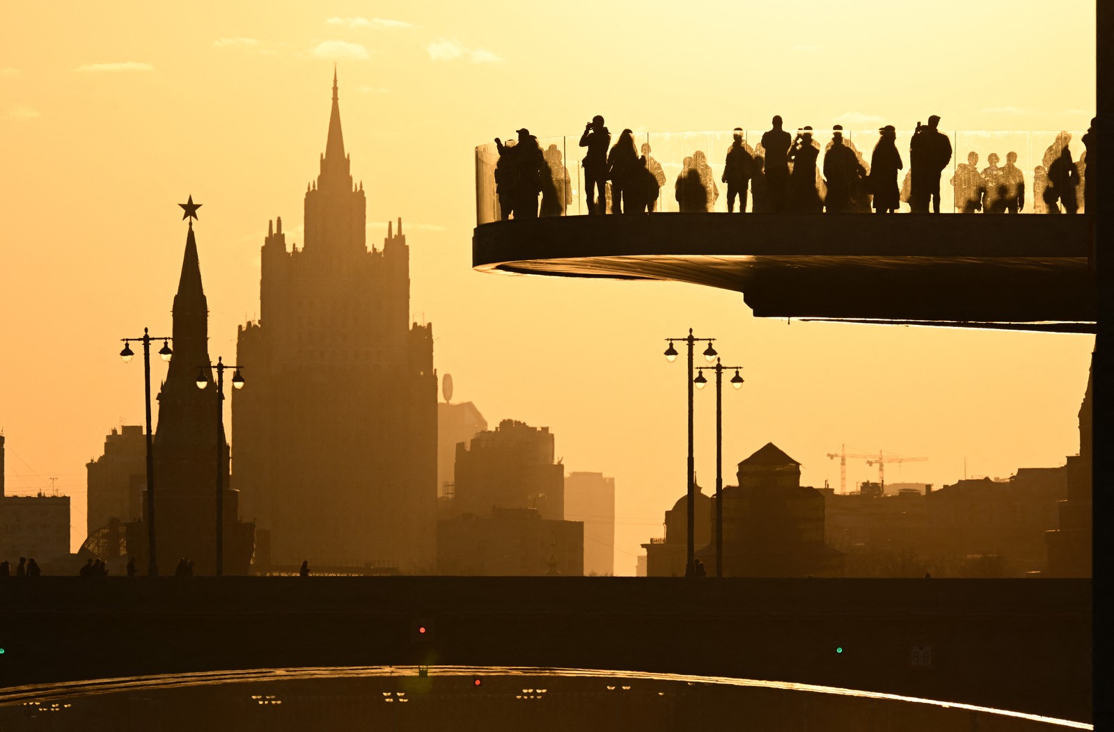 People stand on a cantilevered bridge at sunset, with a view of Moscow in the background.