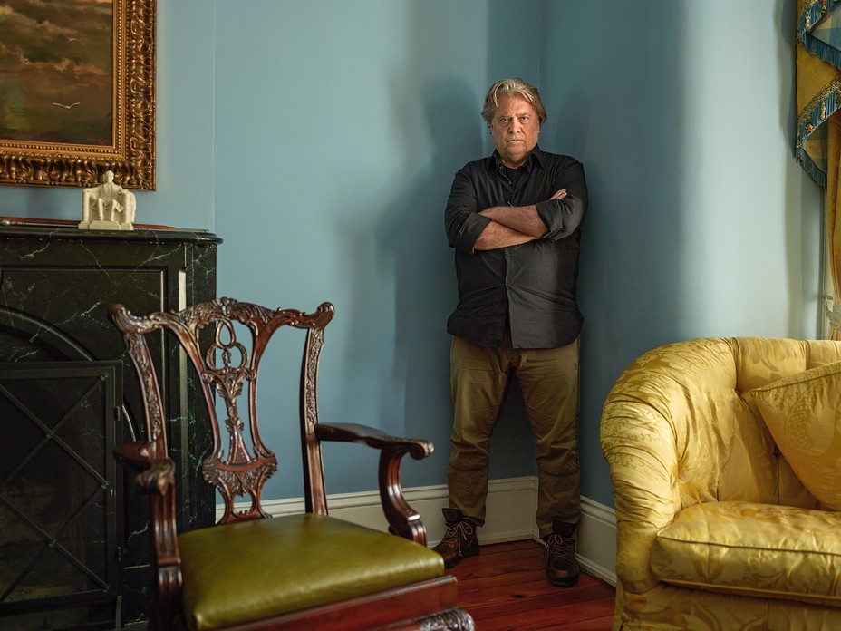 Bannon standing in corner of blue-green room, arms crossed, near overstuffed yellow sofa and antique chair