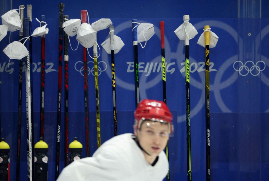 About a dozen protective face masks are seen hanging from hockey sticks that have been set along a wall during a practice session.