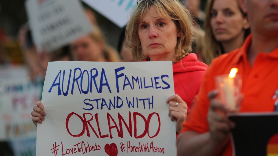 A woman at a candlelight vigil holds a sign reading "Aurora families stand with Orlando."